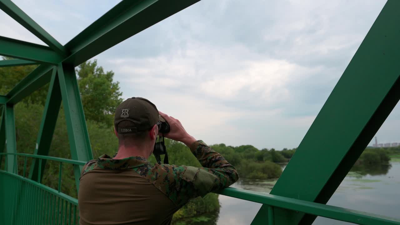 Uomo che guarda nel telescopio su un ponte sopra il lago