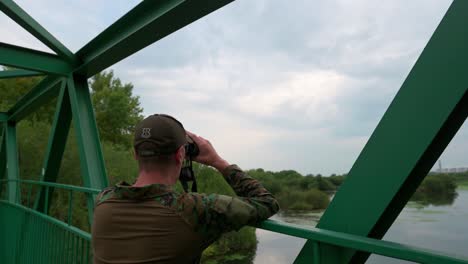 Man-looking-into-the-telescope-on-a-bridge-over-the-lake