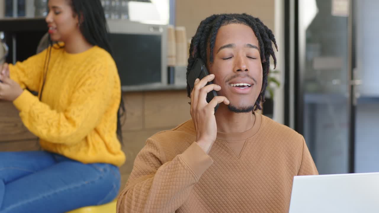 African American man sitting by laptop at office getting alert tapping smartphone calling back