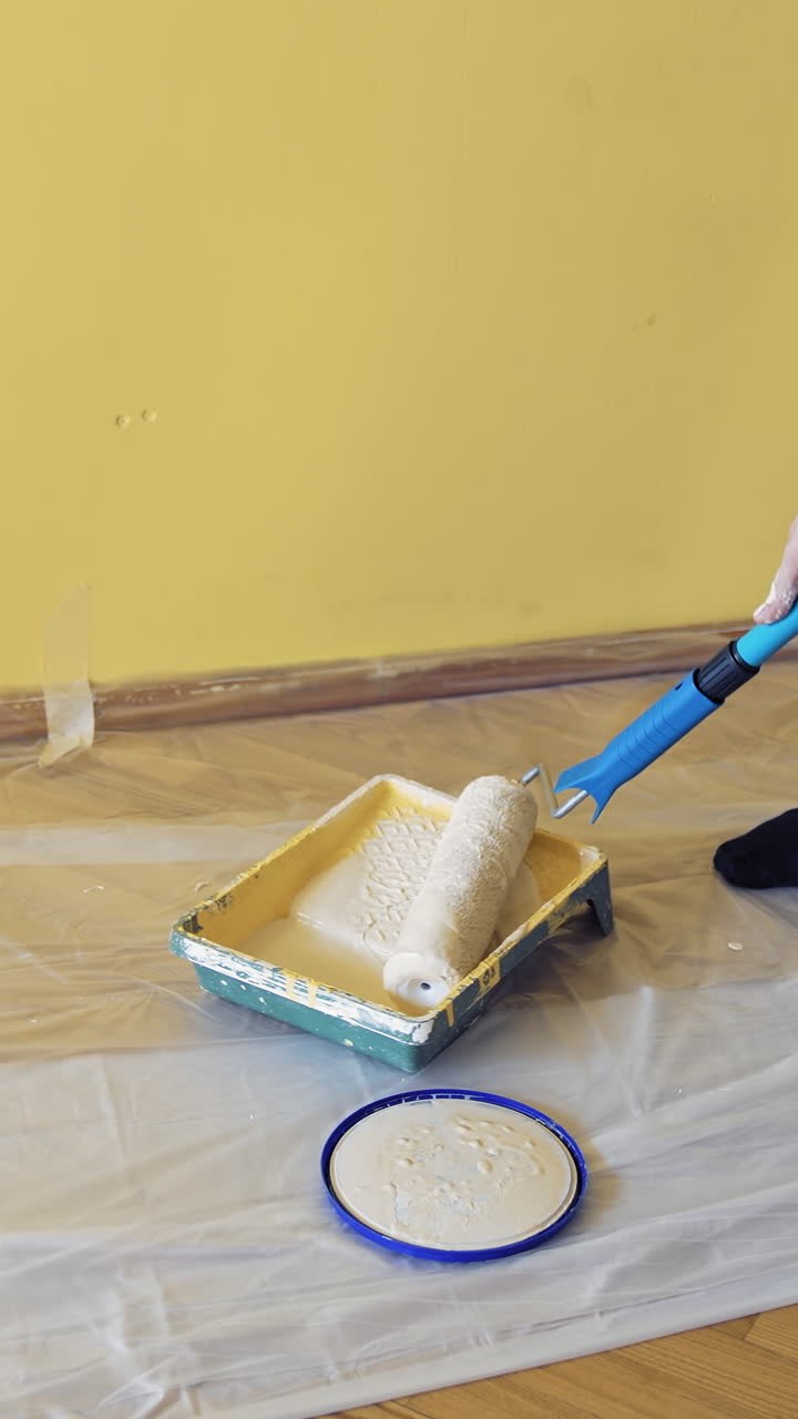 Worker get paint on a roller paint before the renovation. Man taking new color on a paintbrush in a paint tray to decorate walls in the apartment. Vertical video