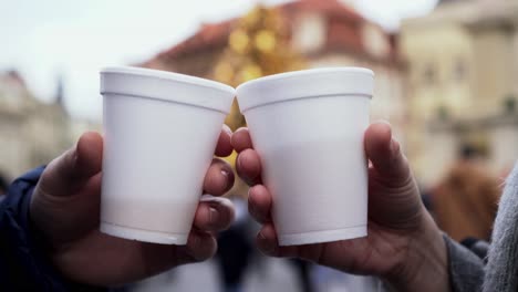 clinking plastic cups with hot steaming wine, christmas tree and blurry lights in background, closeup view