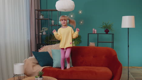 niña feliz niña con auriculares bailando y saltando mientras escucha la música en casa sola