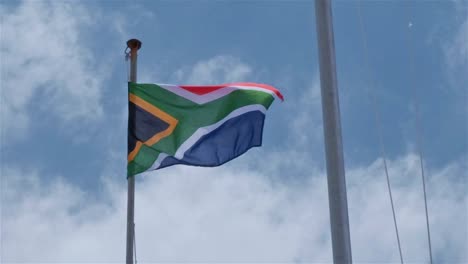 bandera sudafricana soplando en el viento en un poste de bandera con un cielo azul y nubes