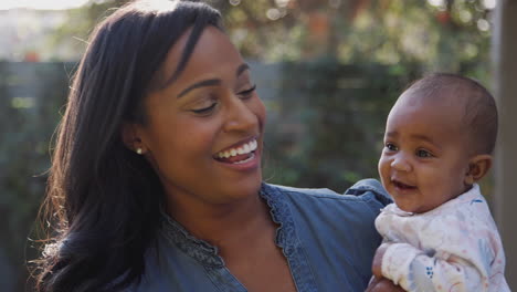 Portrait-Of-Smiling-African-American-Mother-Cuddling-And-Playing-With-Baby-Daughter-In-Garden