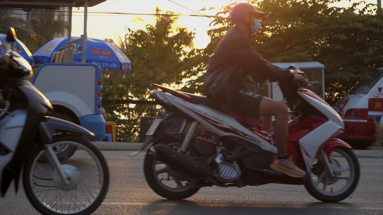 As the sun sets in Phu Quoc, local traffic flows along the road, creating a vibrant atmosphere. The golden light reflects off the pavement, showcasing the beauty of the island.