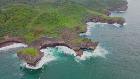 aerial view of an island overgrown with dense forest with coral cliffs and big waves