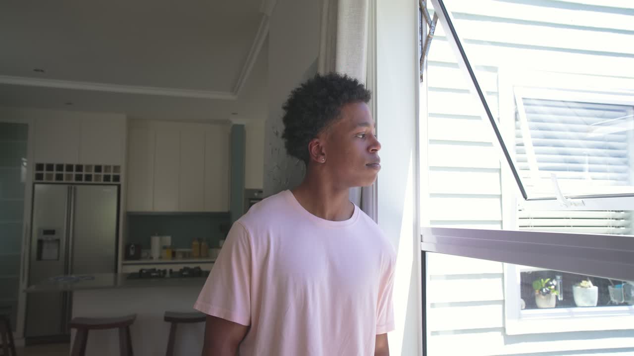 African American man standing by awning window at home sun drawing gaze turning smiling with watch