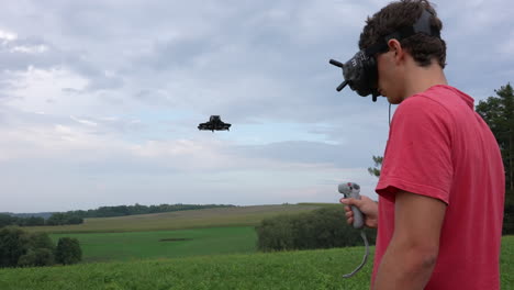 joven con gafas, auriculares y controlador de movimiento que controla el dron fpv en la naturaleza