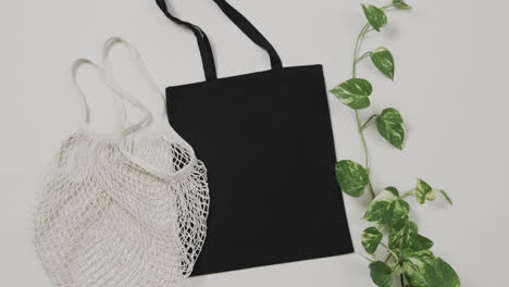 Close-up-of-white-and-black-bags-with-green-plant-on-white-background,-with-copy-space,-slow-motion