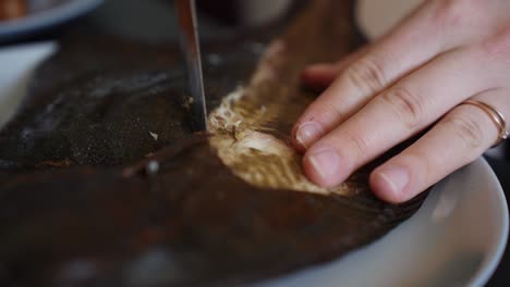 hands of person with golden ring cutting fish fillet to eat, close up view