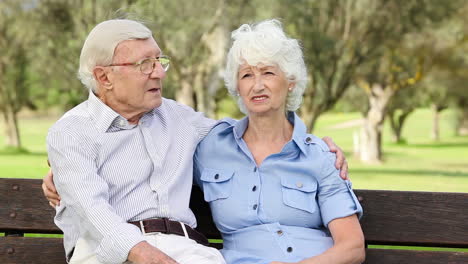 una pareja de ancianos en un banco hablando.