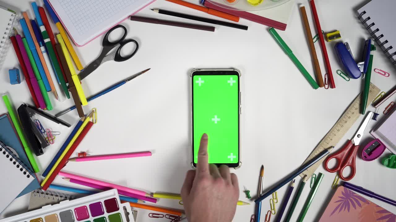 composición de accesorios escolares que rodean el teléfono inteligente con pantalla verde y hombre tocando en la pantalla