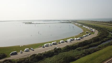 fila de campistas estacionados y gente haciendo windsurf en brouwersdam en los países bajos durante un día de verano