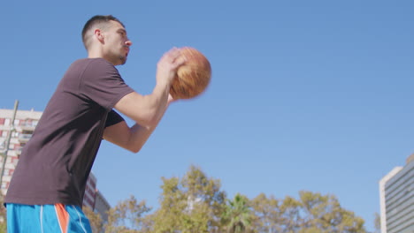 Slow-motion-medium-shot-of-a-young-Caucasian-man-passing-the-ball-between-his-legs-and-shooting-a-basket-on-a-street-basketball-court-in-Barcelona,-Spain