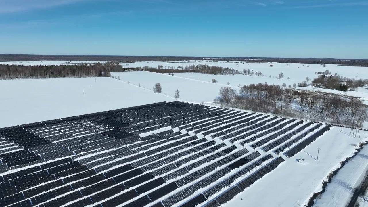 Dron letící nad panely solární elektrárny v řadě na zasněžených polích. Haljala, Estonsko