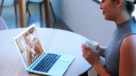 Creative-business-woman-holding-coffee-cup-having-a-video-meeting-on-her-laptop