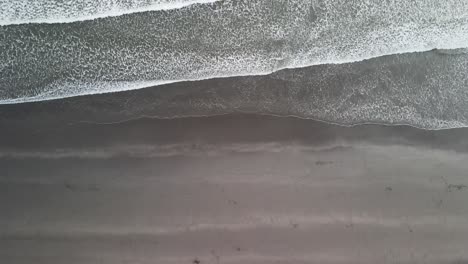 Top-down-view-of-waves-rolling-onto-black-sand-beach-in-New-Zealand