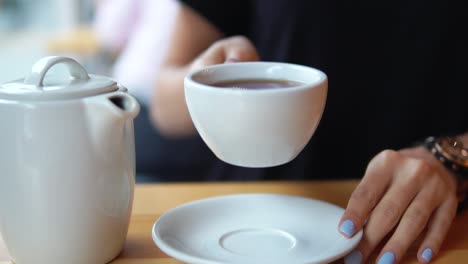 close up view of female hands taking a white cup with hot tea from the wooden table. then camera moves up with a cup and this