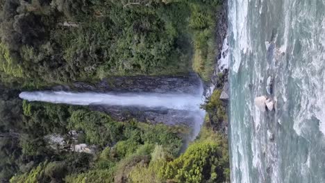 vista vertical de las famosas cataratas de thunder creek rodeadas de selva tropical y el río alimentado por el glaciar que fluye delante de ella en la costa oeste de haast, nueva zelanda.
