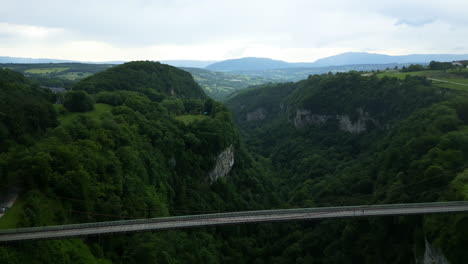 Aerial: gorge with green trees and Caille Bridge during the day with cloudy sky in Allonzier-la-Caille Cruseilles, Haute-Savoie, France, pull out drone shot