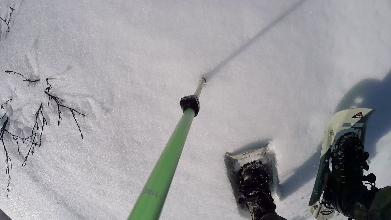 una cámara de acción filmada de un excursionista de invierno usando raquetas de nieve escalando una montaña con un bastón de trekking en la isla de kodiak, alaska