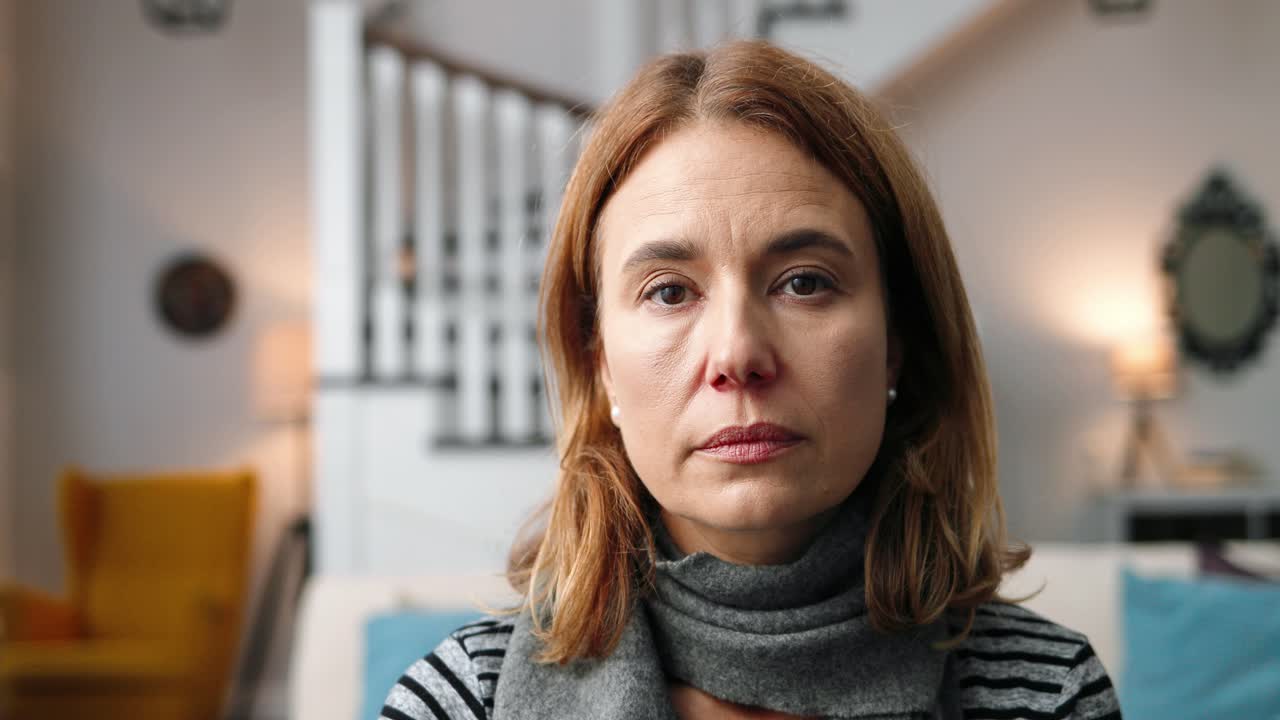 Close up of beautiful middle-aged woman sitting at home and looking at camera