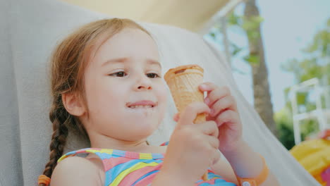 A-Happy-Little-Girl-Enjoys-Summer-Vacations-Lies-On-A-Couch-At-Sea-And-Eats-A-Delicious-Ice-Cream