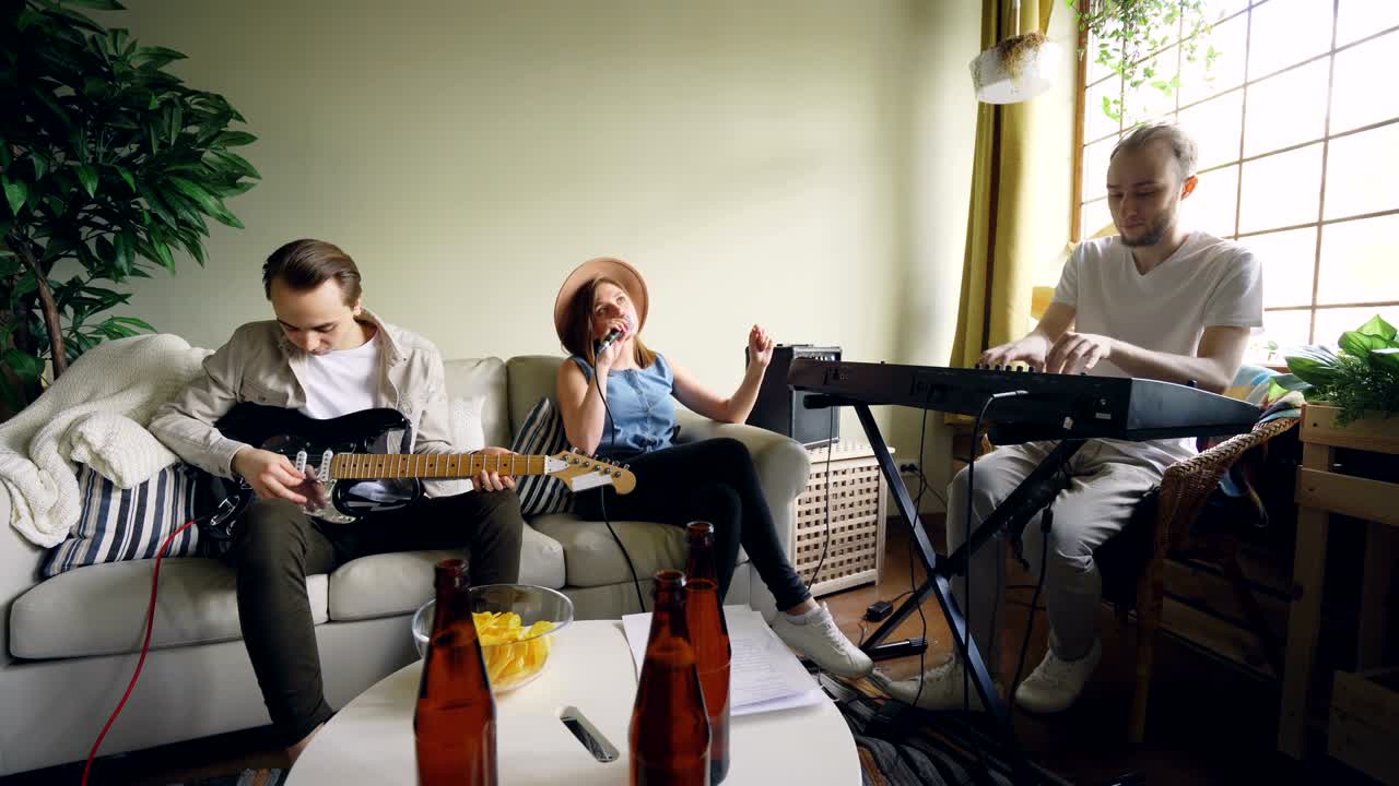 Two cheerful guys musicians are playing keyboard and guitar while their female friend vocalist is singing holding microphone. Friendship and music concept.