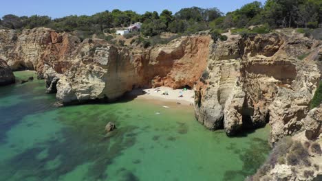 un dron vuela desde detrás de los acantilados oceánicos para revelar a la gente en una playa privada secreta rodeada de aguas turquesas tropicales del océano