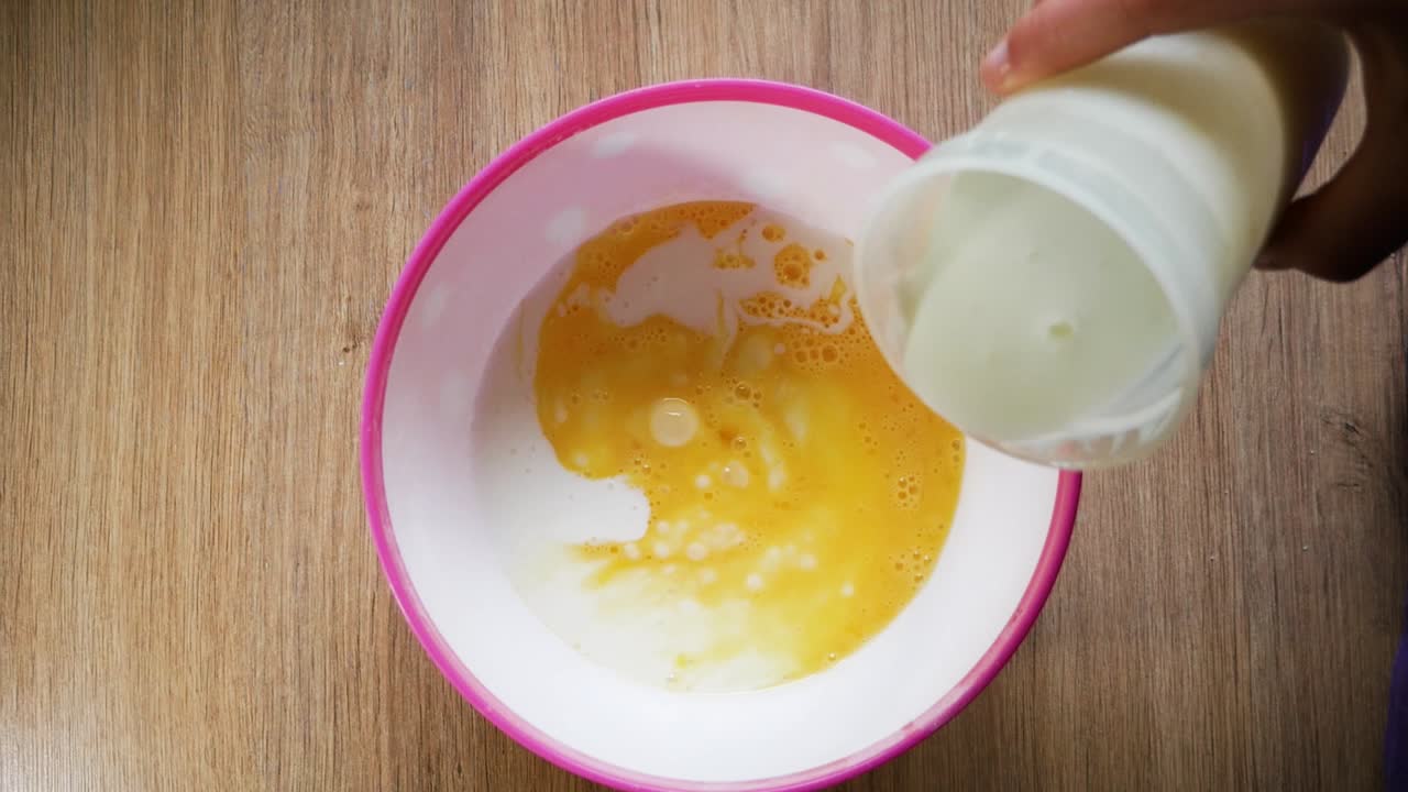 Pouring milk into whipped egg for American pancake preparation.