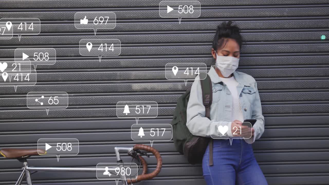 Animation of social media icons and numbers on banners over woman in face mask using smartphone