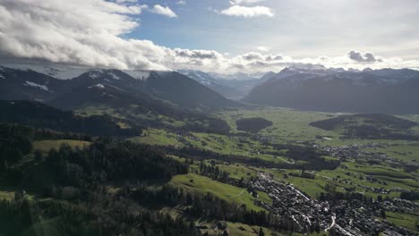 hermosa fotografía cinematográfica de drones en círculo de picos de montañas cubiertos de nubes y aldea de abajo, suiza, de día