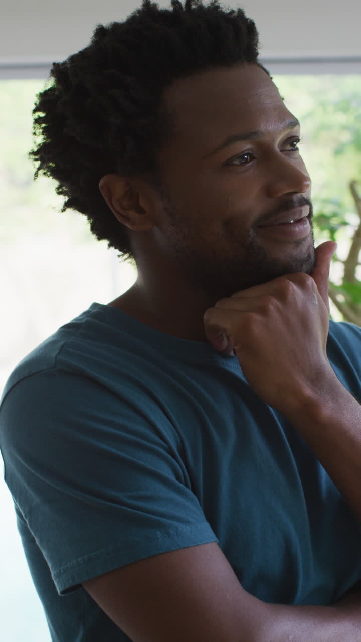 Ritratto video verticale di un uomo afroamericano pensieroso che guarda altrove sorridendo a casa