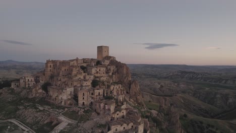 Drohne-Fliegt-In-Großer-Kreisbewegung-Um-Die-Ruinen-Von-Craco-Auf-Einem-Hügel-Mit-Dem-Sonnenaufgang-Im-Hintergrund-In-4k