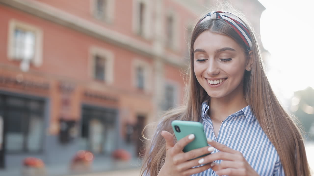 Giovane donna che reagisce con sorpresa e gioia mentre usa lo smartphone su una strada cittadina