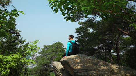 Hombre-Excursionista-Descansando-En-Una-Gran-Roca-Montañosa-Disfrutando-Viendo-El-Majestuoso-Horizonte-De-La-Ciudad-De-Seúl-Desde-Gwanaksan-En-Un-Hermoso-Día-De-Verano---Muñeca-En-Cámara-Lenta