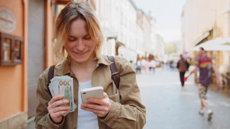 woman counting money dollar cash using smartphone calculator app satisfied of salary on city street