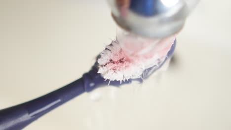 closeup of a toothbrush being rinsed under running water in a sink