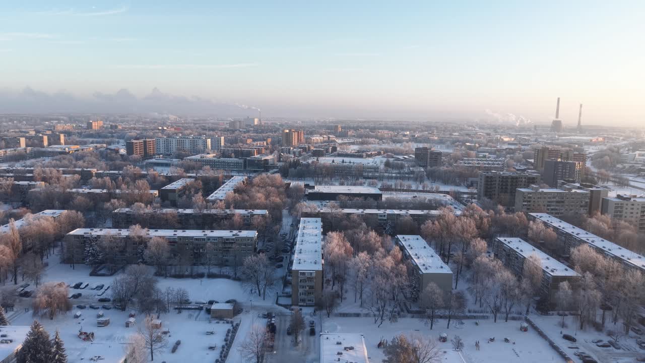 Dronevideo, der fanger et fredfyldt, snedækket bybillede ved daggry, og viser frostklædte træer, boligblokke og industribygninger under et blødt morgenlys
