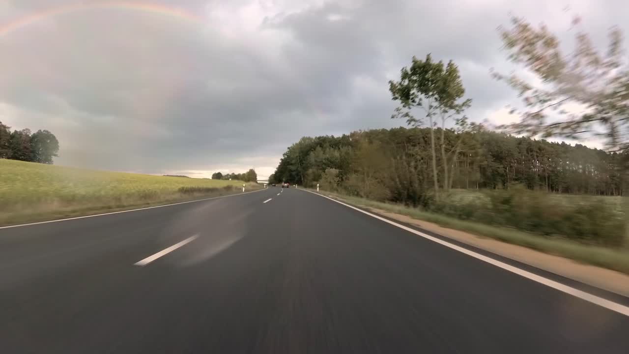 First person view of driving over a german highway on a rainy day seeing a rainbow in front, 4k
