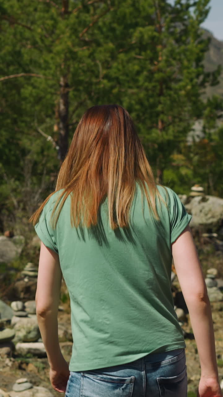 Redhead woman walks to stacked stones near pine forest backside view slow motion. Spiritual power and meditation. Altai mystical traditions
