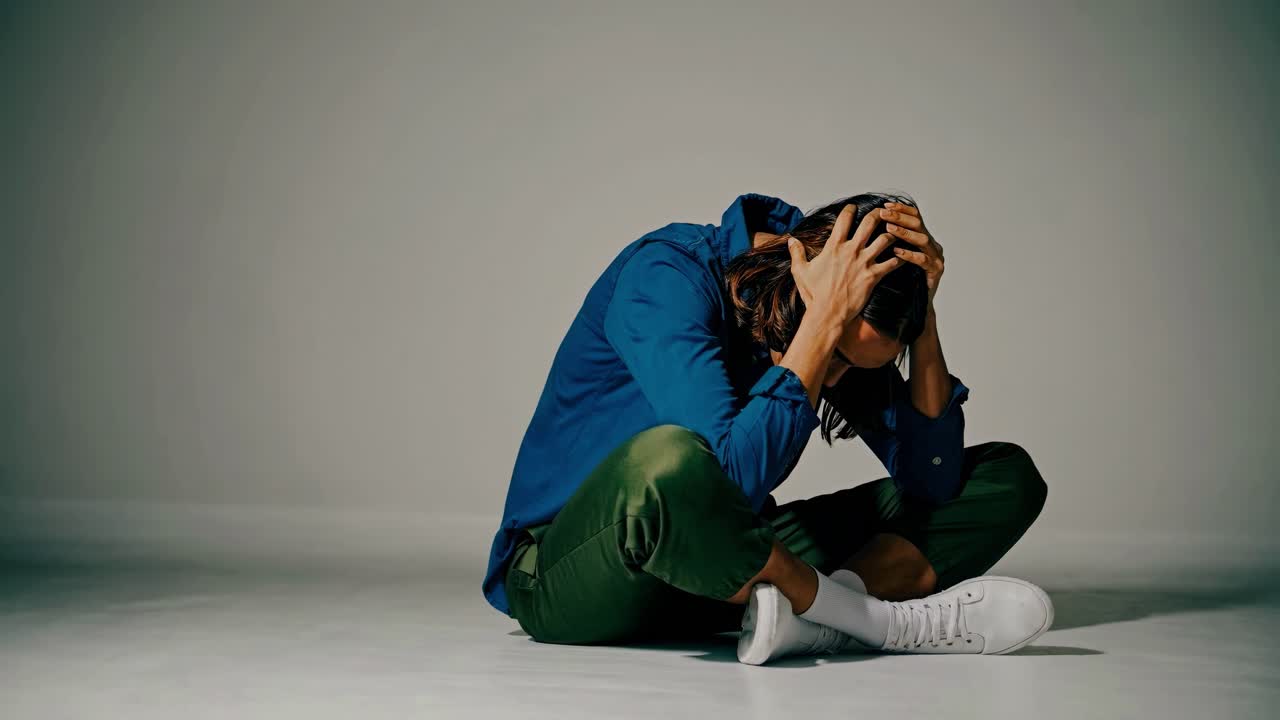 A dramatic video scene shows a person sitting on the floor, head in hands, captured from a low