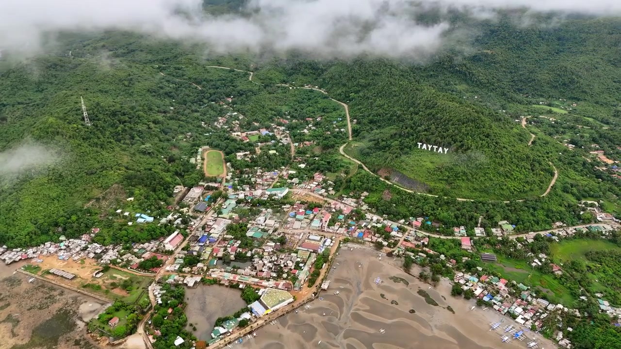 Poblacion, Taytay, Palawan, Filipinler'de, alçak bulutlar altındaki Taytay kasabasının, beyaz TAYTAY yamaç tabelası harfleri, yoğun konutlar ve koy kıyı şeridi ile yüksek irtifa hava görünümü.