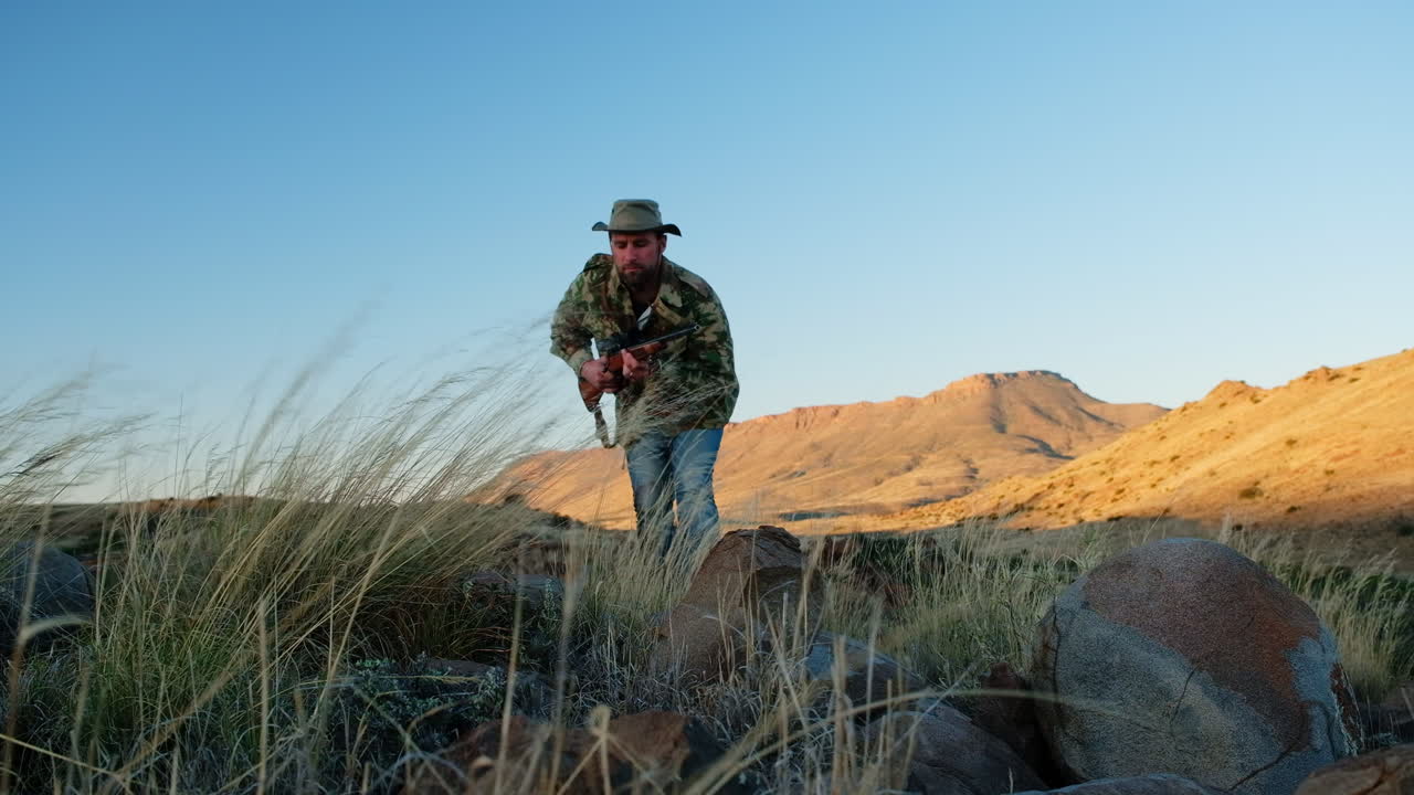 Cazador con rifle de caza en mano acecha presa sobre rocoso paisaje de Karoo