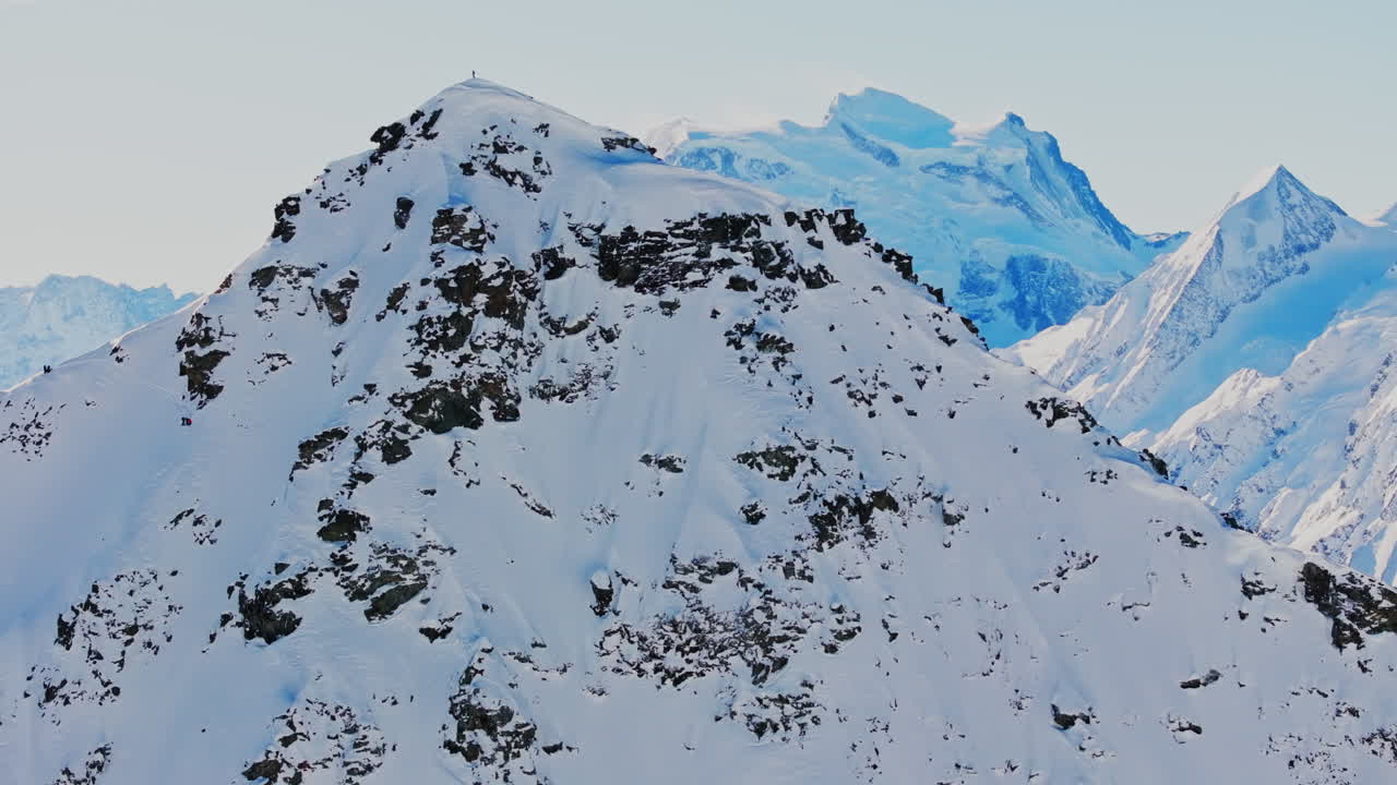 Freeride skier stands on the summit of the legendary Bec des Rosses, gazing over the stunning alpine panorama with the Grand Combin towering in the background