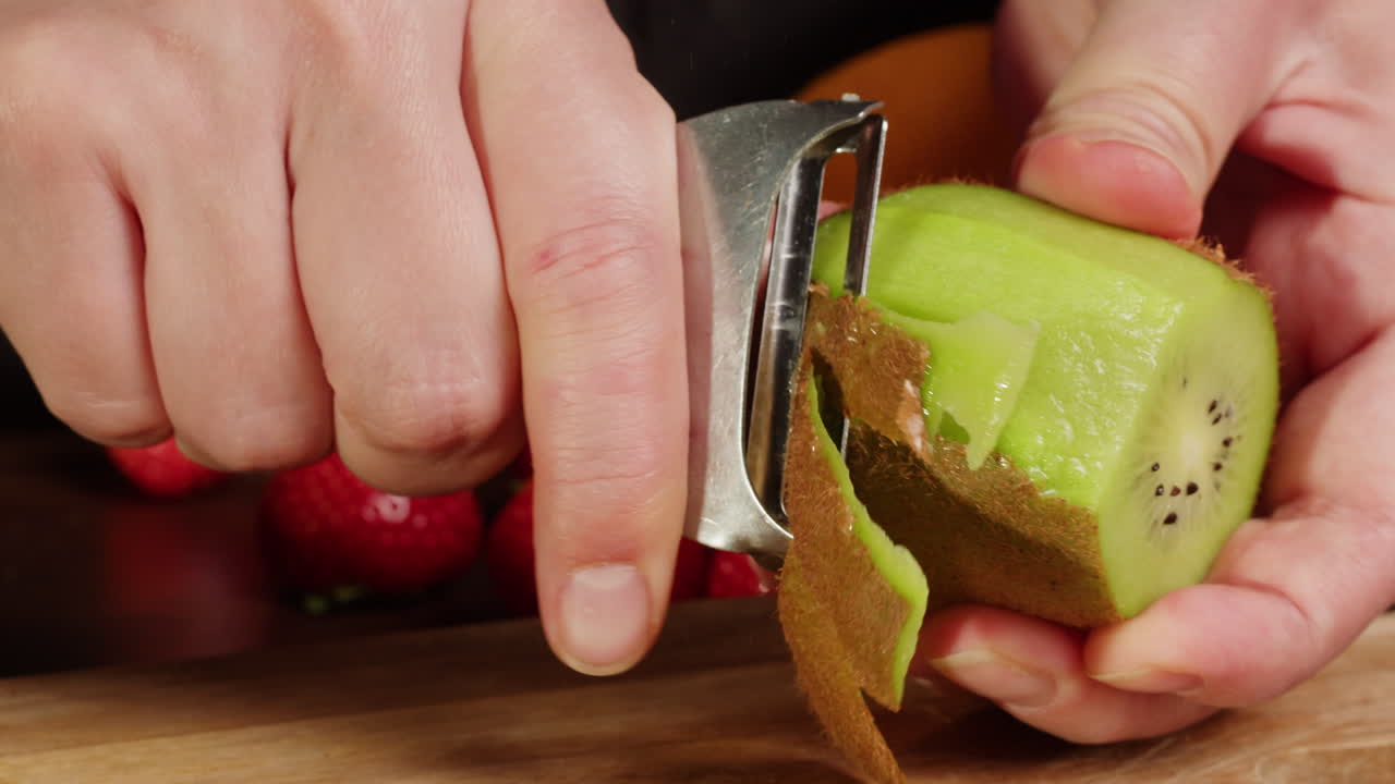 Close-Up of Hands Peeling a Fresh Kiwi Fruit with a Peeler