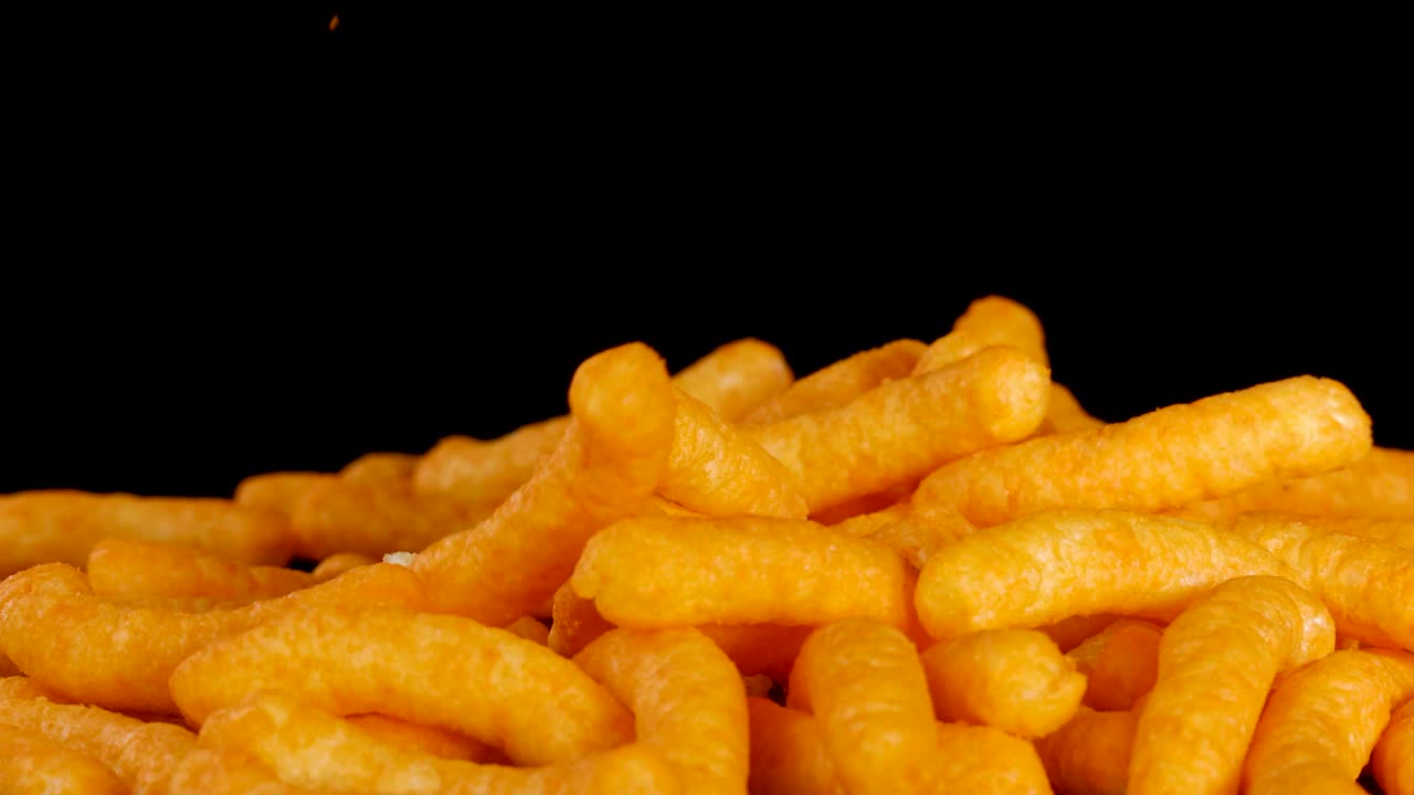 Cheese puffs fall onto a pile, brightly lit, with crisp detail and black background