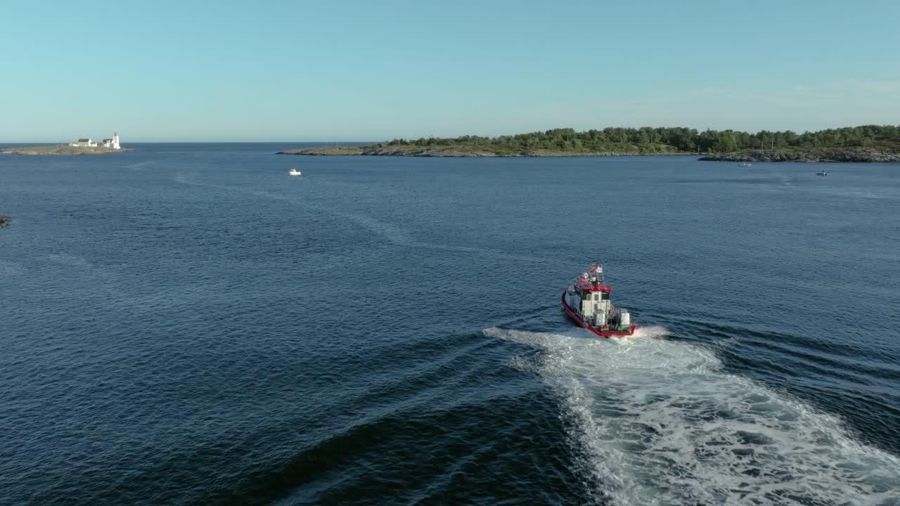 A tugboat maneuvers through tranquil waters near several small islands under a clear sky. The setting sun casts a warm glow on the scene, illuminating the coastline
