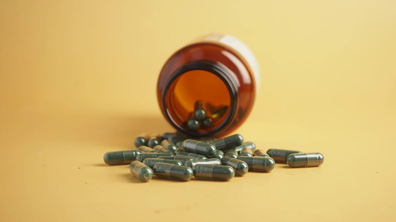 Dark Green Capsules Spilling from a Brown Bottle on Yellow Background