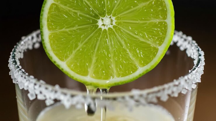 Un primo piano vibrante di una fetta di lime fresco che gocciola succo su un bordo di vetro smerigliato, catturando perfettamente l'essenza delle bevande rinfrescanti agli agrumi.